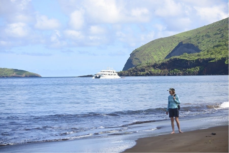 Person on a Galapagos beach and a cruise ship.